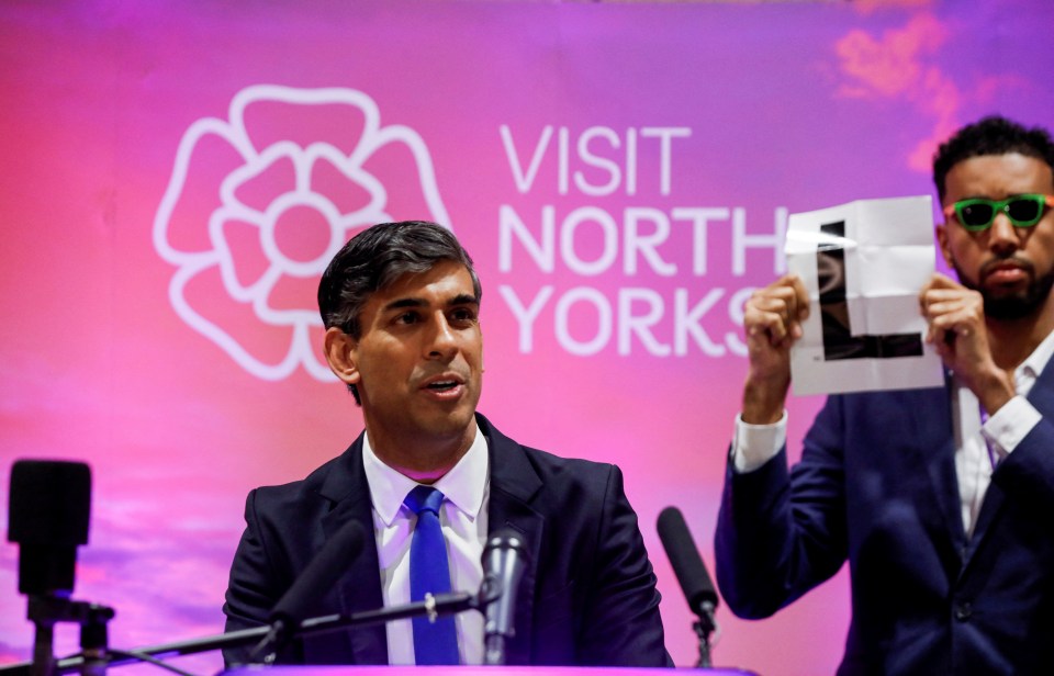 In an idiotic stunt Niko Omilana held up an 'L' behind Rishi Sunak as he delivered a speech on July 5, 2024