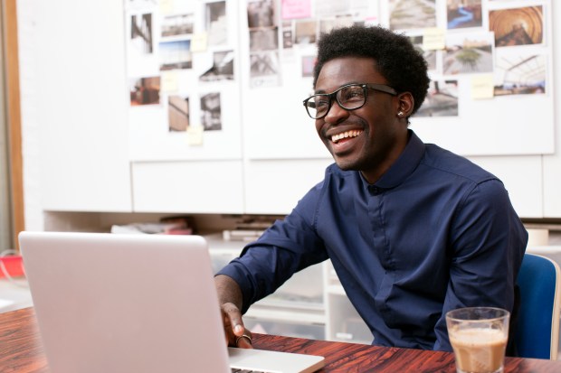 a man wearing glasses is smiling while using a laptop