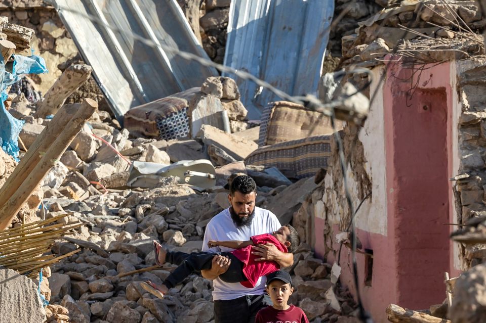 A man carries a boy through the devastation of the quake rubble behind another lad