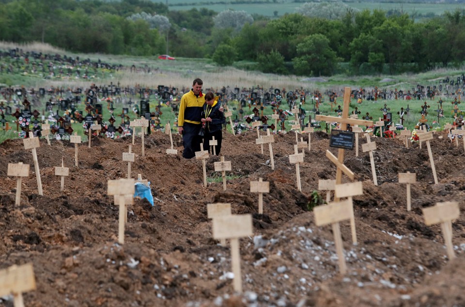 People stand among newly-made graves at a cemetery in bomb-blizted Mariupol