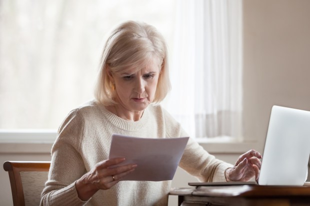 a woman is looking at a piece of paper while using a laptop