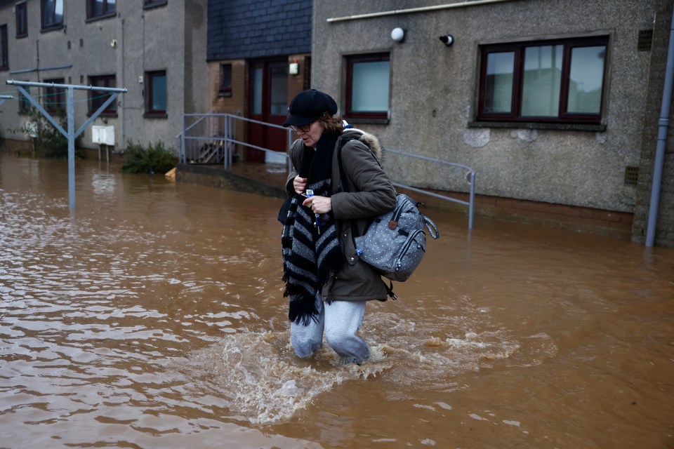 A woman wades through the flood waters near some houses in Brechin