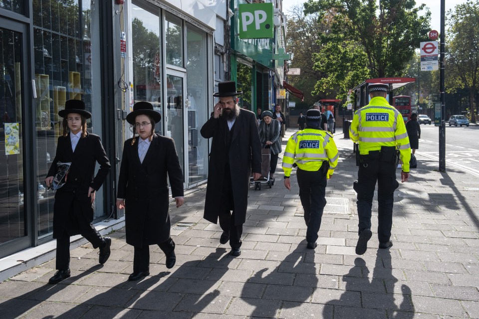 Orthodox Jewish men pass police officers as they patrol around Stamford Hill, north London