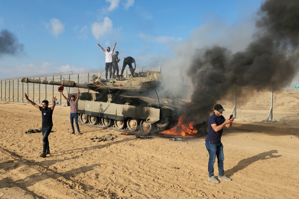 Palestinians celebrate by a destroyed Israeli tank at the Gaza Strip fence