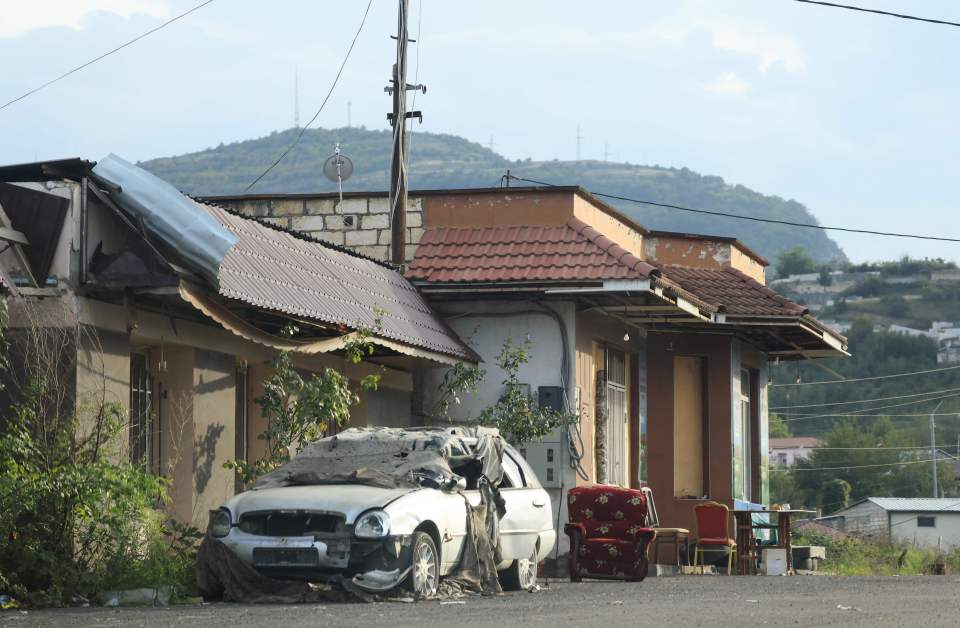 A partially destroyed car lies next to abandoned chairs