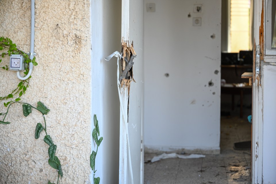 Bullet holes are seen on the walls of a house next to a broken door handle