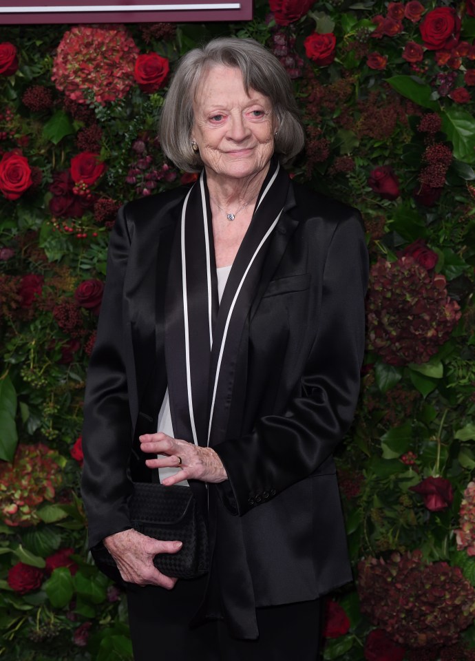 a woman in a black suit stands in front of a wall of flowers