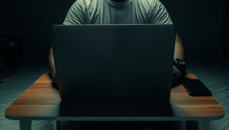 A man in a white shirt sits on a laptop in a dark room. with light shining down. internet concept addiction.topview.