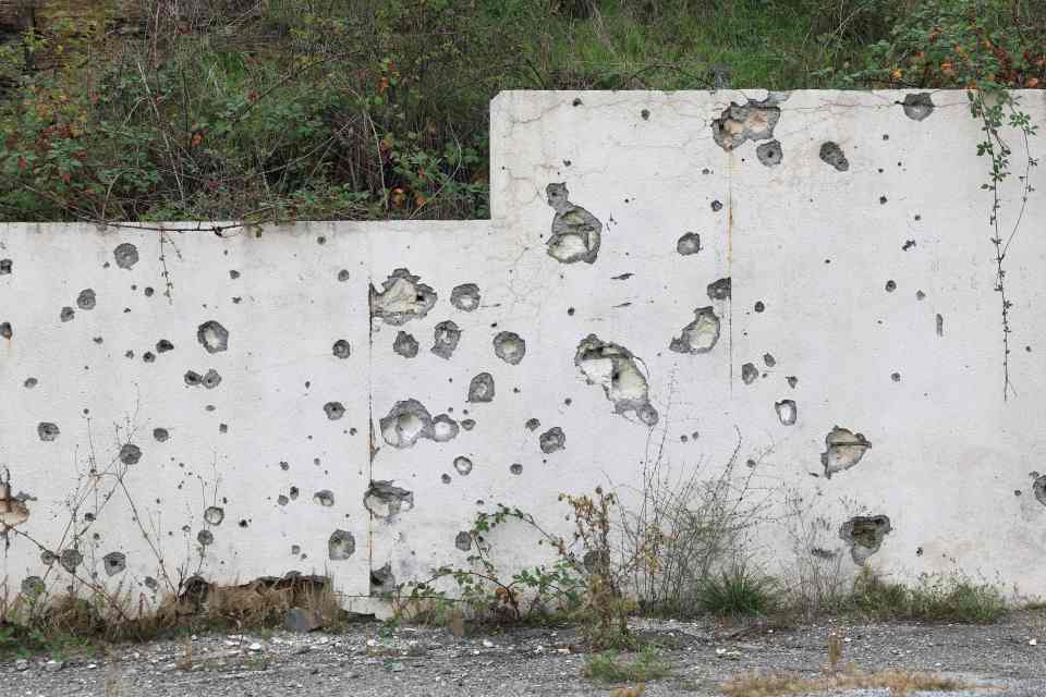 A wall marked with shrapnel and bullet holes in the road entering Stepanakert