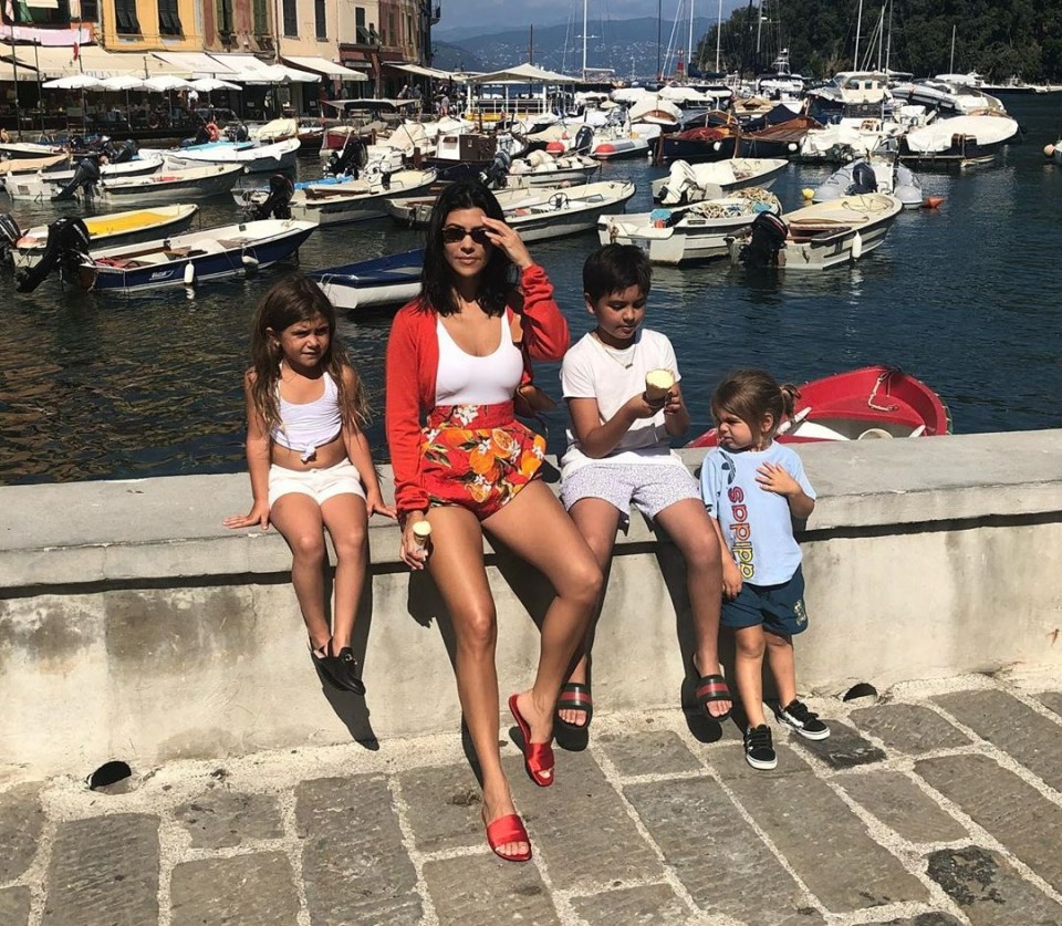 a family sits on a wall eating ice cream with boats in the background