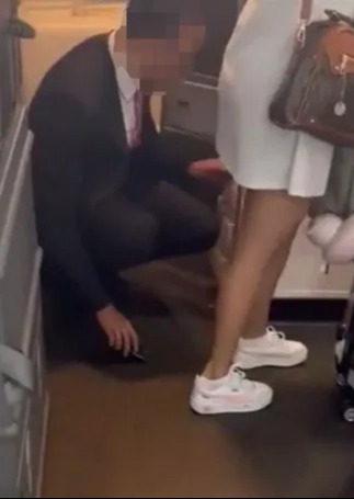 The man appears to slide his phone, camera up, across the floor as she walks past