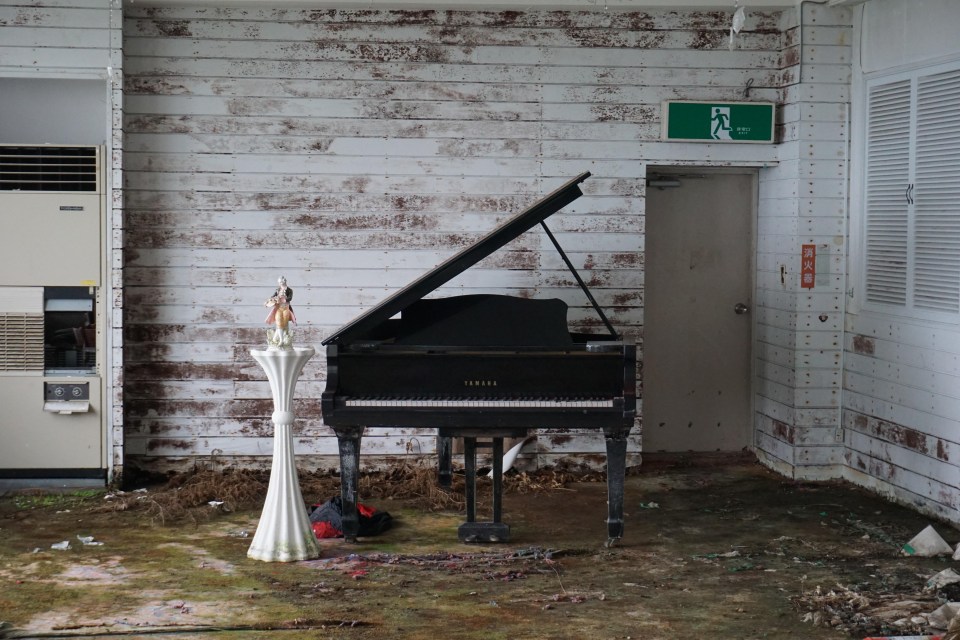 A grand piano sits alone in a white decaying room