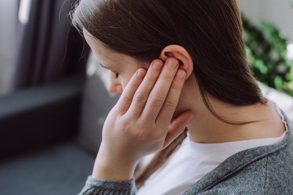 Tinnitus concept. Close up up of sick young caucasian female touch plug ear suffer from noisy disturbing sound sitting on sofa at home. Annoyed millennial lady having earache, hearing problems