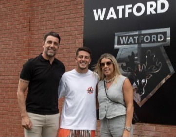 three people are posing for a picture in front of a watford sign .