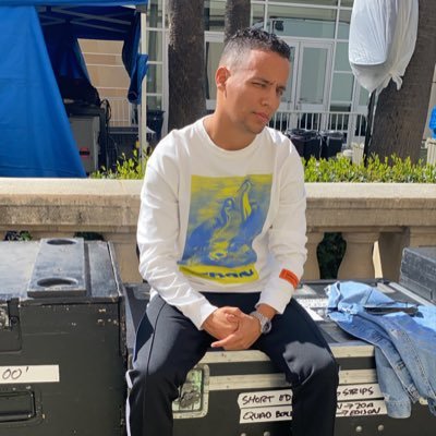 Man in white sweatshirt with bird graphic sits on equipment crates.