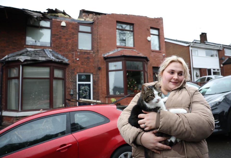 A local resident holds her cat in front of a house damaged in Greater Manchester