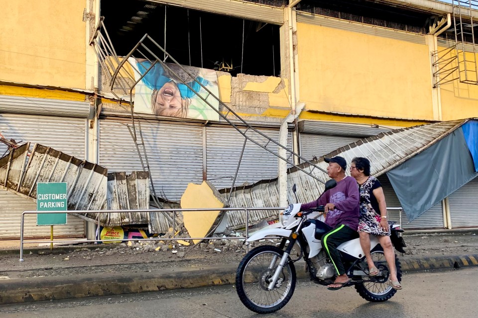 A motorcycle passes by a partially damaged grocery store caused by the tremors on Sunday morning