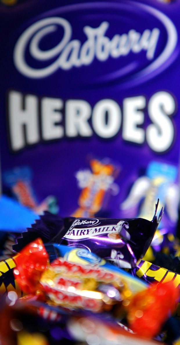 a box of cadbury heroes candy sits in front of a pile of candy