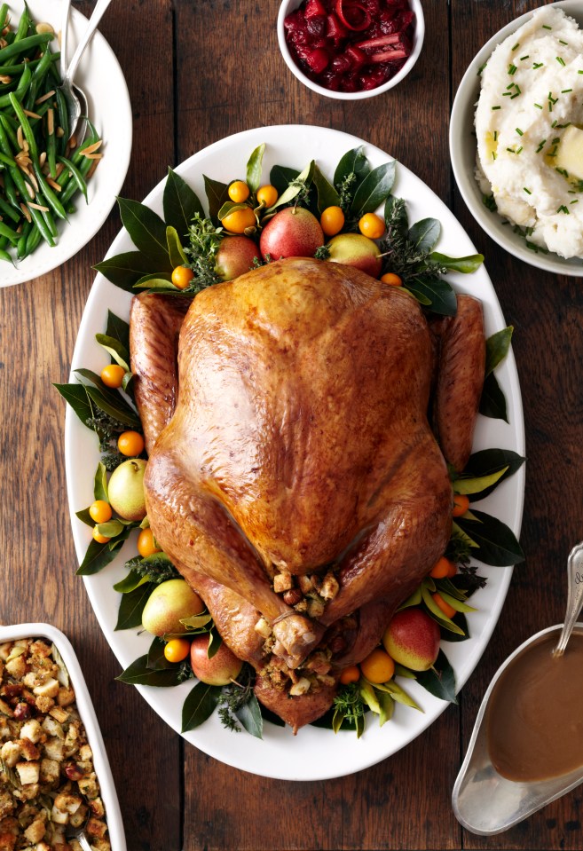 Roasted turkey garnished with fruit and herbs, surrounded by Thanksgiving side dishes.