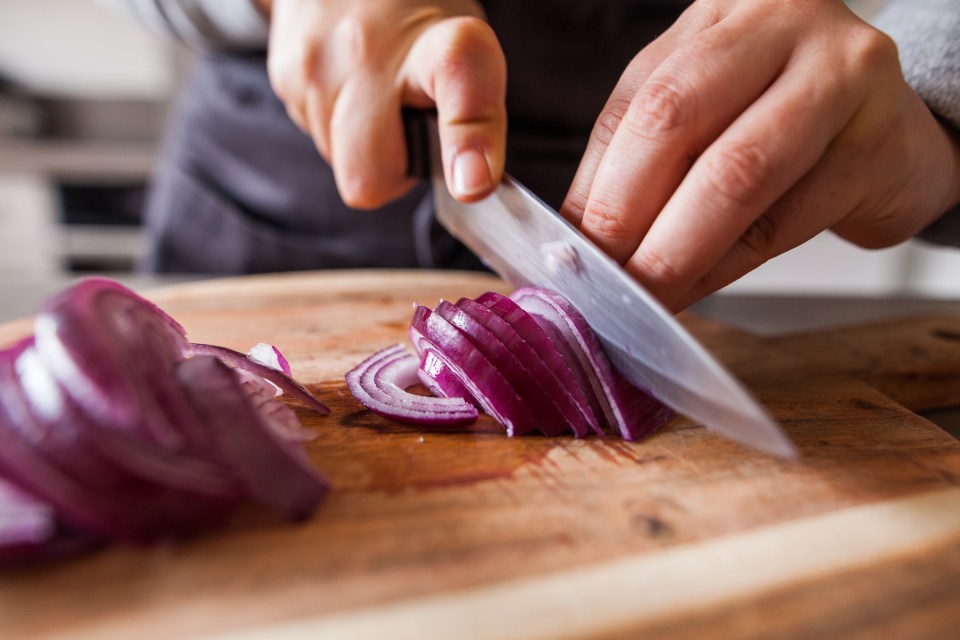 Person slicing red onion on wooden cutting board.