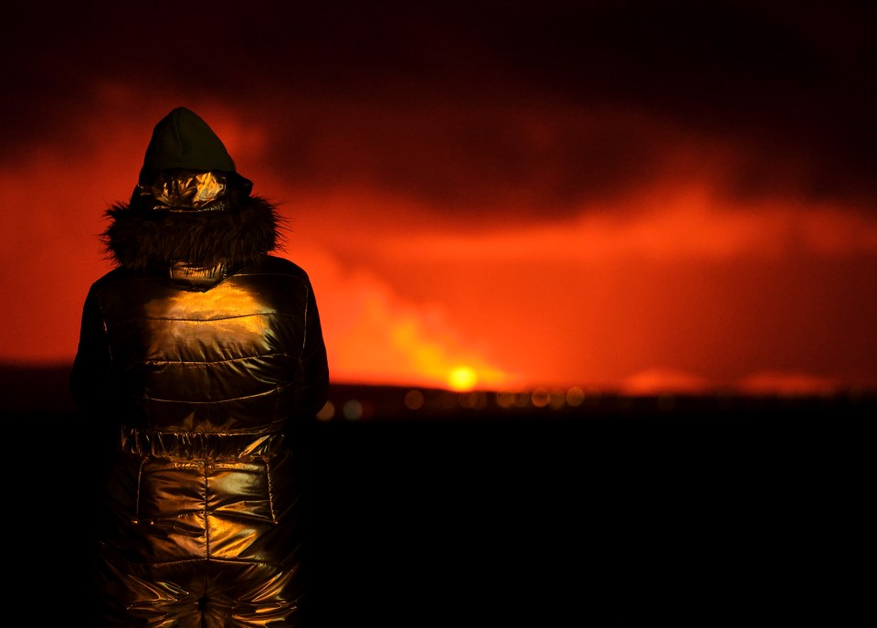 An onlooker stands by the shoreline in Reykjavik to watch as the volcano erupts