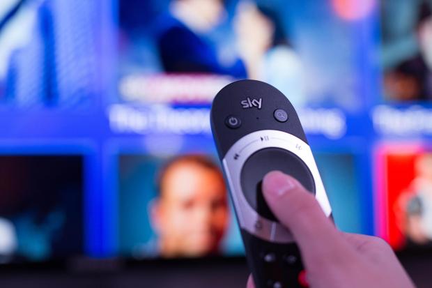 a person is holding a sky remote control in front of a television