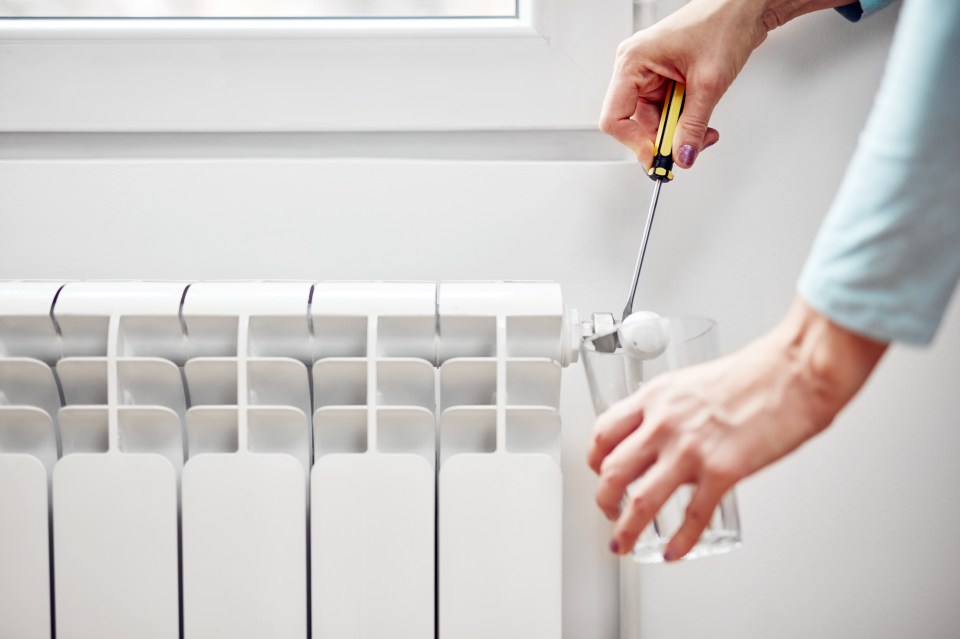 Woman fixing and bleeding air from central heating gas radiator system at home.