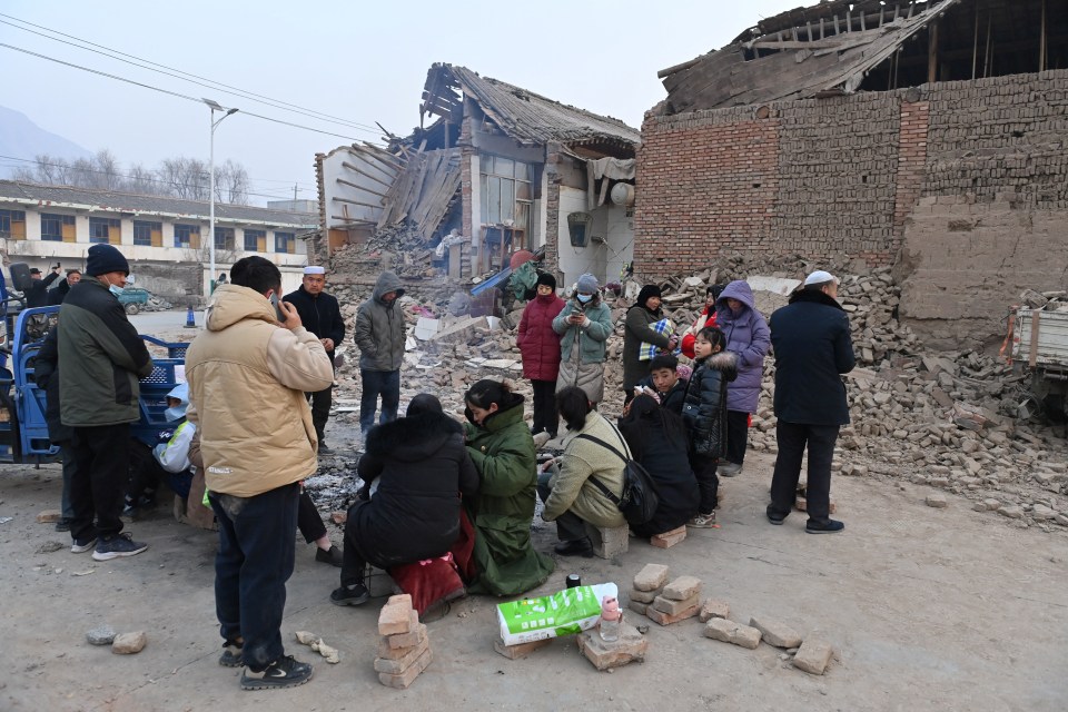 Residents keep warm by a fire in -13C next to buildings damaged by the quake