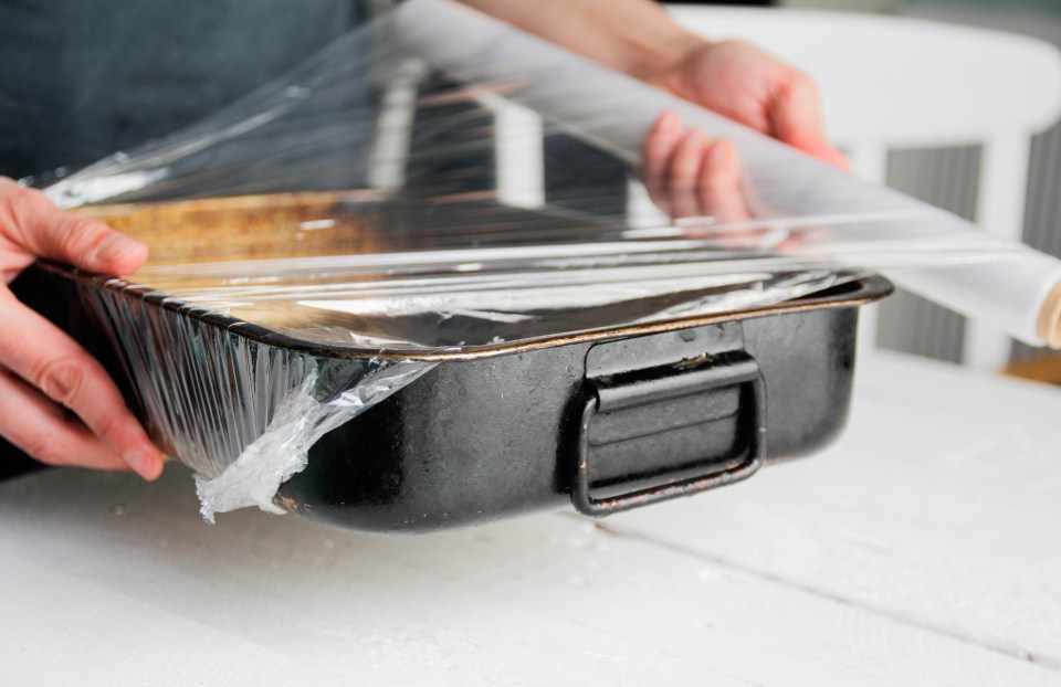 Hands wrapping a baking tray in plastic wrap.