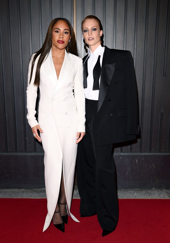 two women in tuxedos pose for a picture on a red carpet