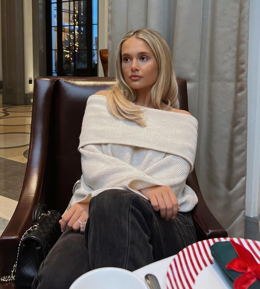 a woman in a white off the shoulder sweater sits in a chair