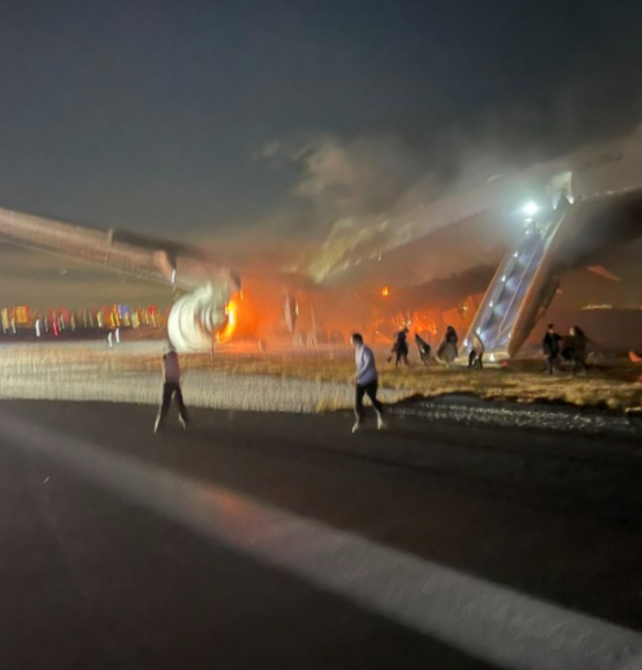 Passengers and crew can be seen evacuating the aircraft at Tokyo's Haneda Airport