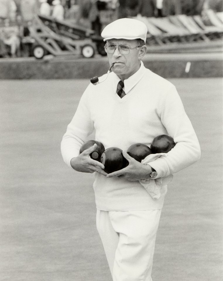 Black and white photo of a man smoking a pipe and carrying bowling balls.