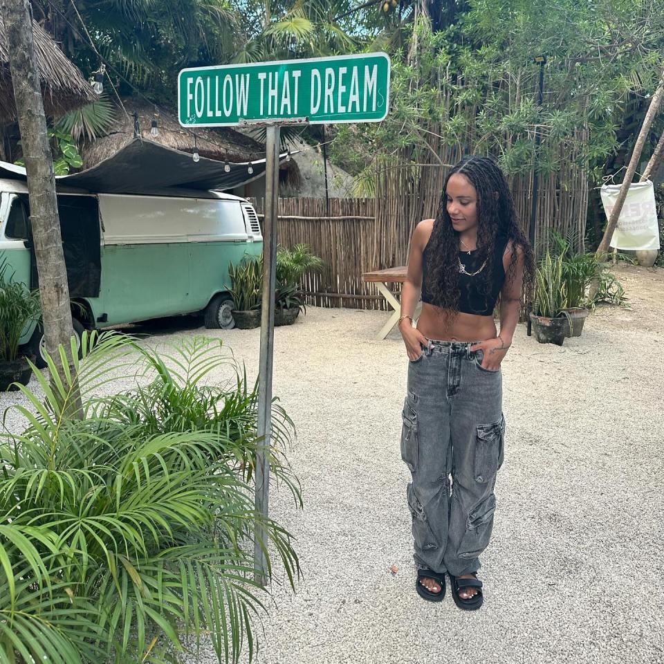 a woman stands in front of a sign that says follow that dream