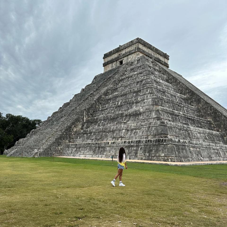 a woman stands in front of a large stone pyramid