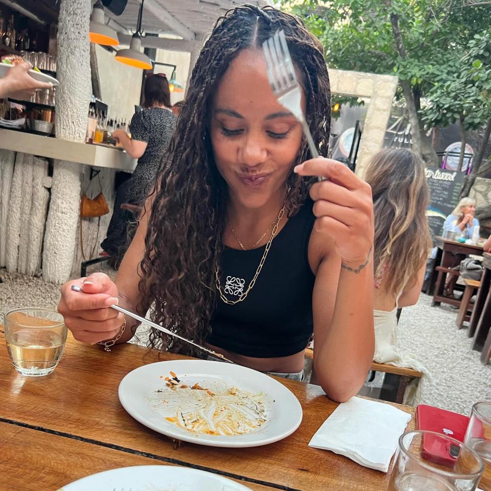 a woman wearing a loewe necklace is eating a plate of food