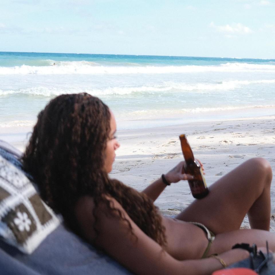 a woman sits on a beach holding a bottle of beer