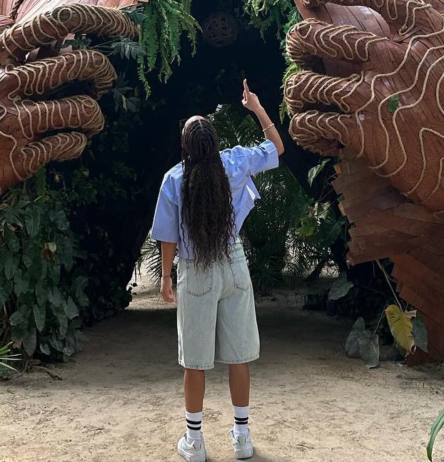 a woman with long hair is standing in front of a wooden sculpture .