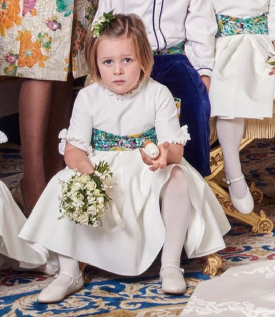 Young girl in white dress holding flowers at a royal wedding.