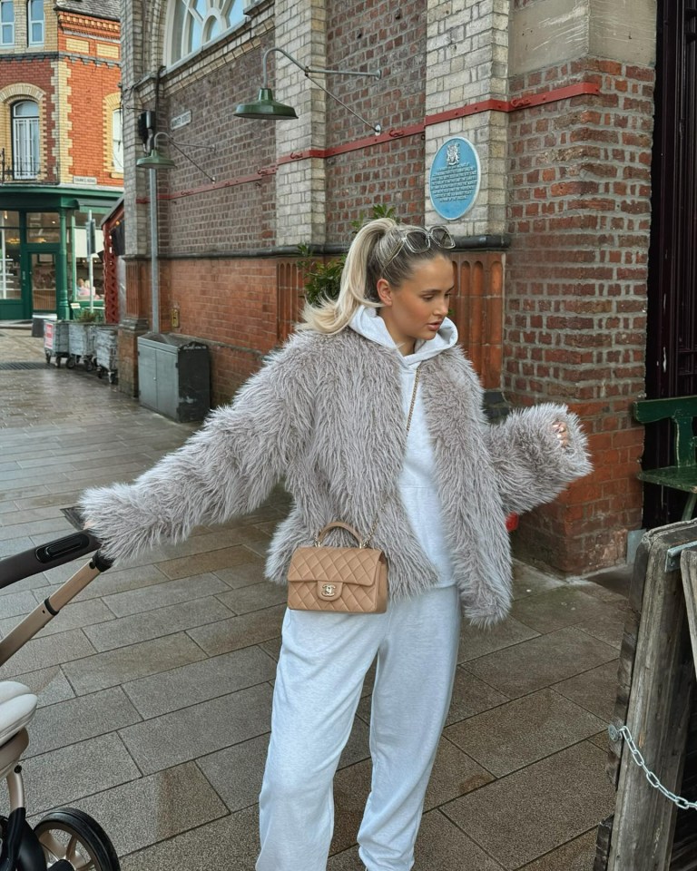 a woman wearing a fur coat stands in front of a brick building