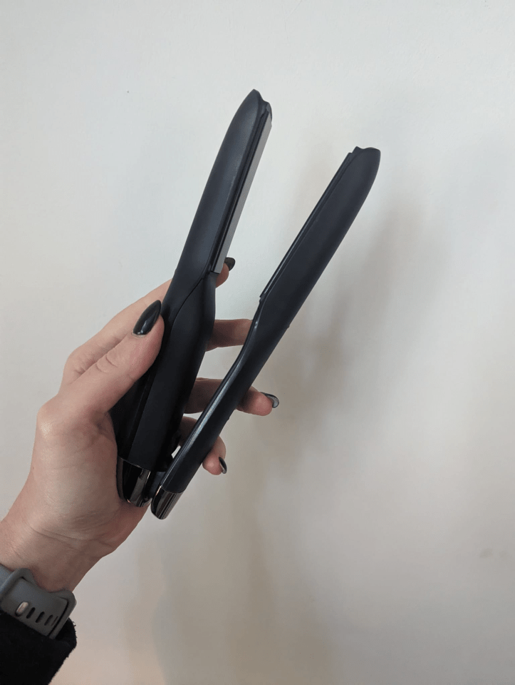 A hand holding two black hair straighteners.