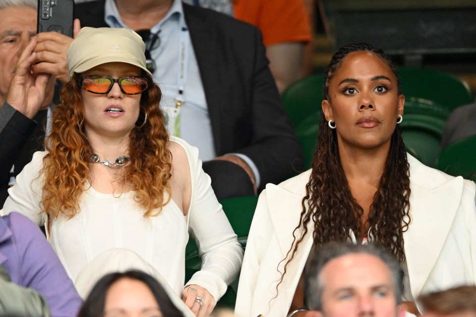 two women sitting in a crowd with one wearing sunglasses