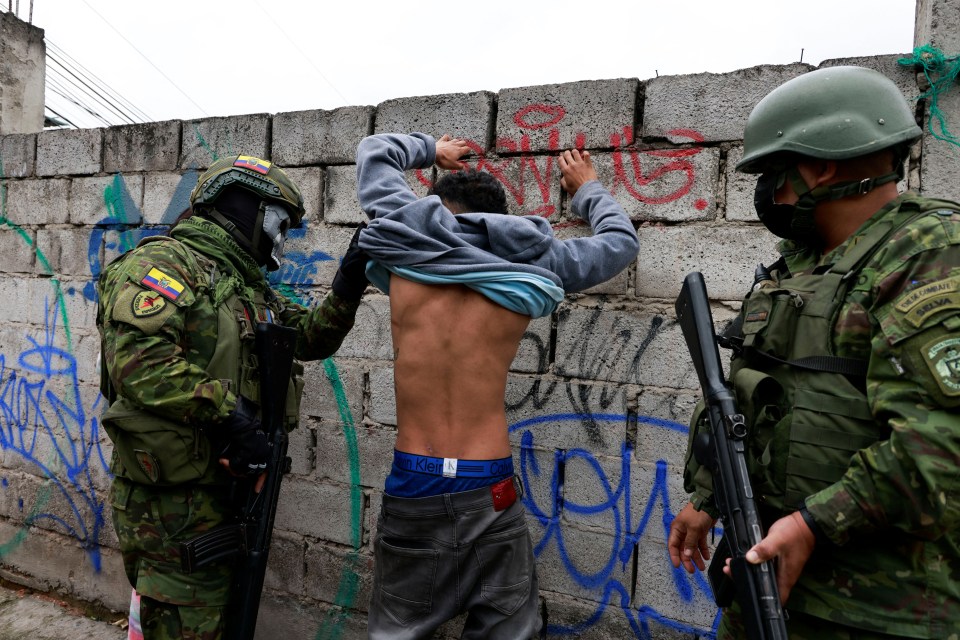 Members of the armed forces of Ecuador check the tattoos of a man on the street for potential gang affiliation during a security operation