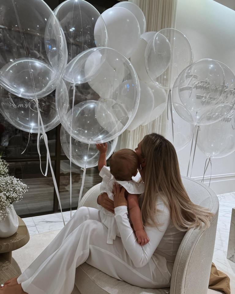 a woman holding a baby in front of a bunch of balloons