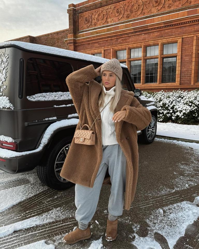 a woman in a teddy bear coat stands in front of a car covered in snow