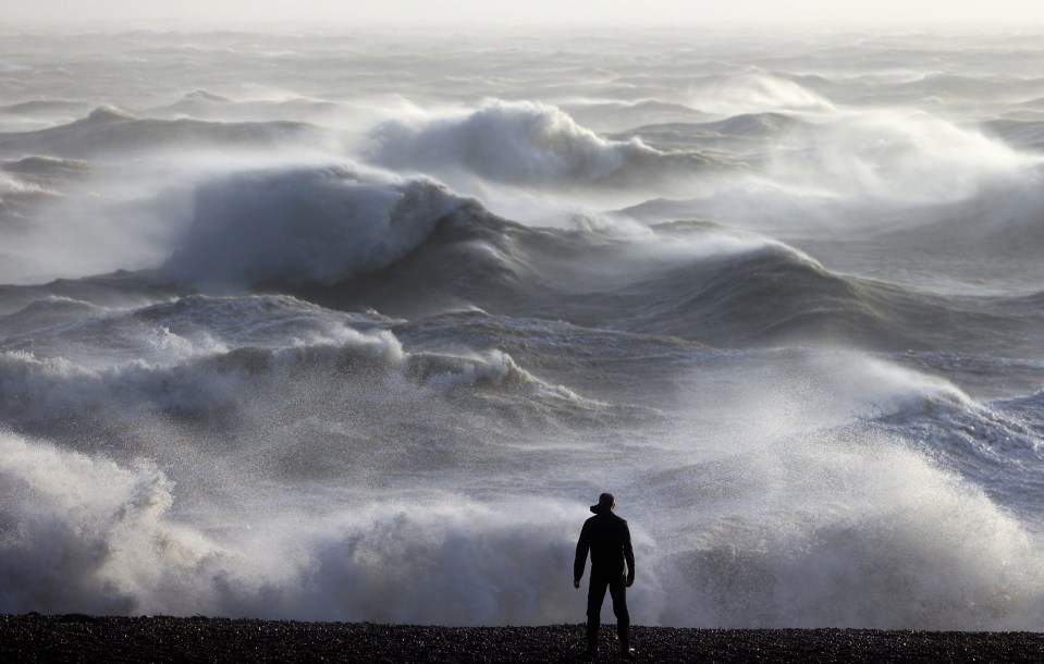 A person looks out towards the waves crashing on the shore in Newhaven today