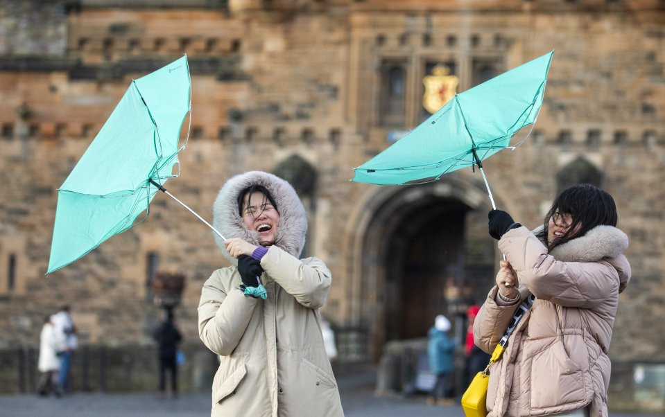 Tourists are buffeted by the wind outside Edinburgh Castle this morning