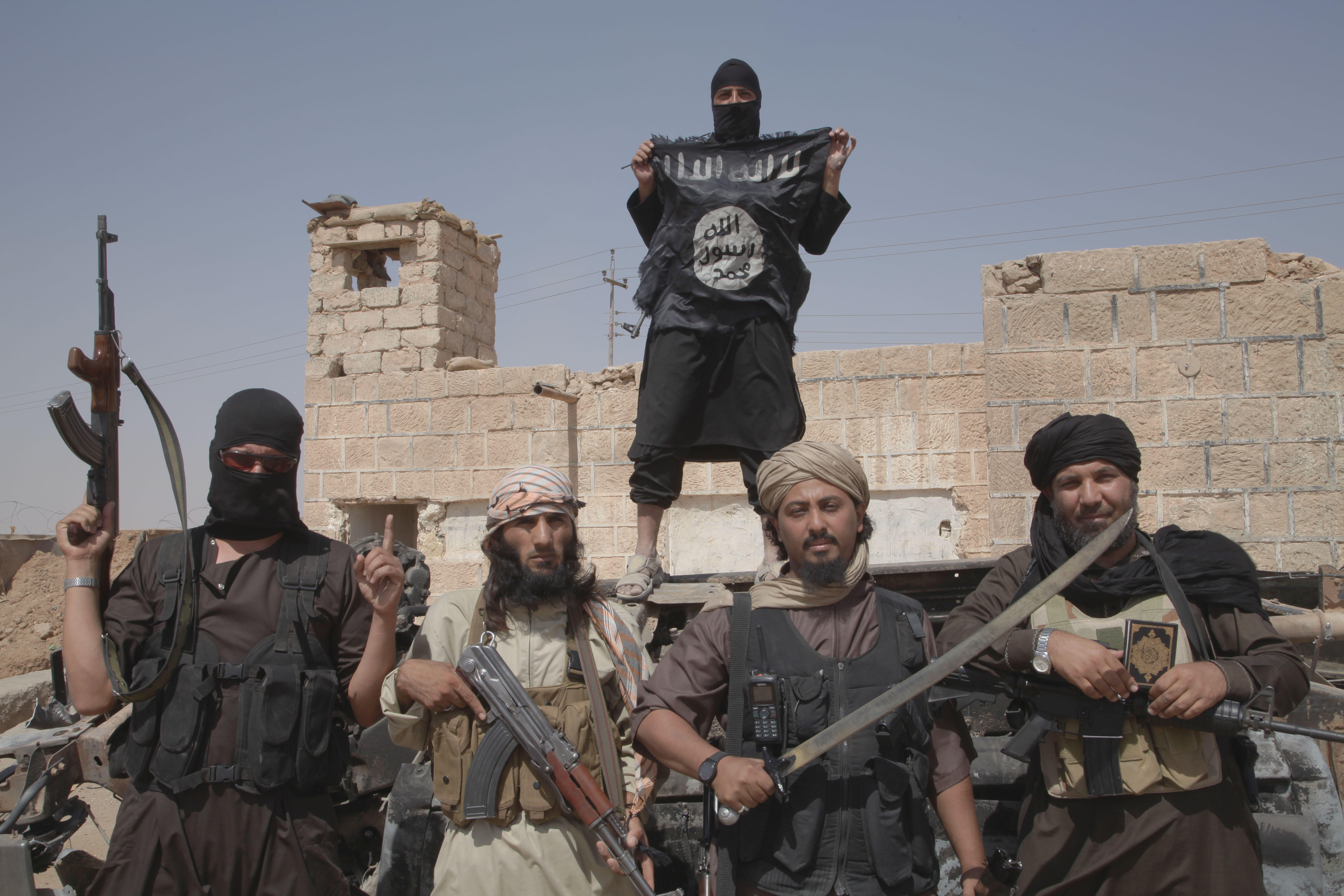 ISIS members brandishing flags, guns and machetes on the border between Iraq and Syria