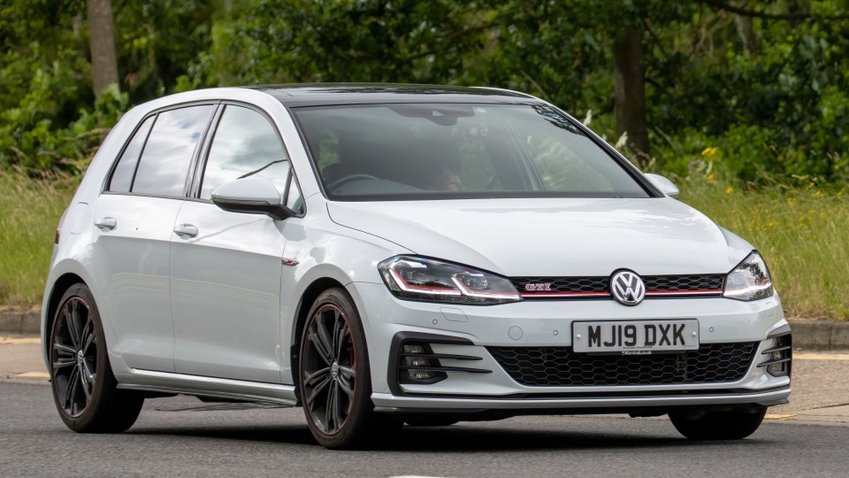 White Volkswagen Golf GTI driving on a road.