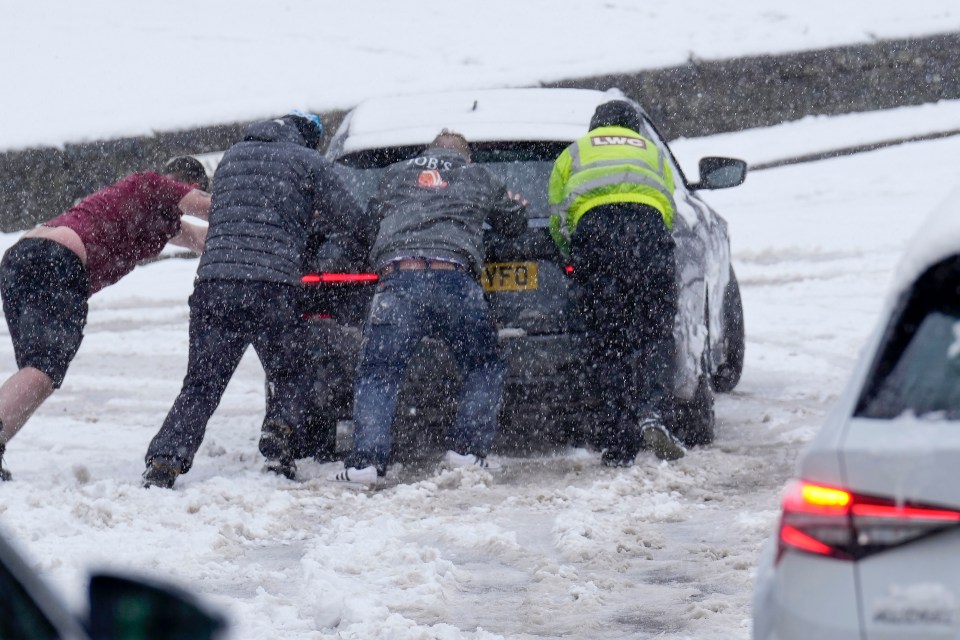 People help to rescue a sliding car in the snow in Buxton